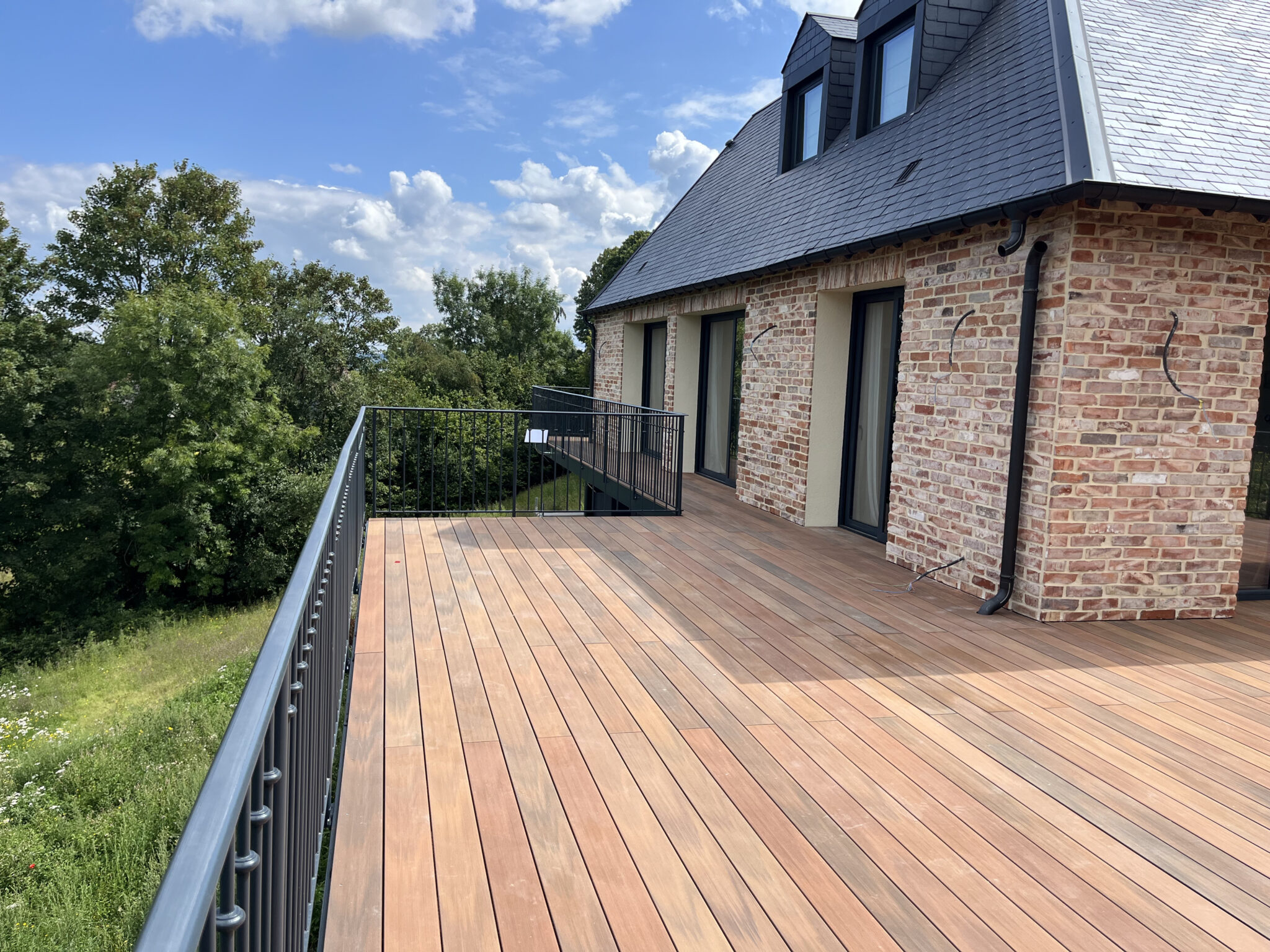 Grande terrasse en bois près d'une maison en brique.
