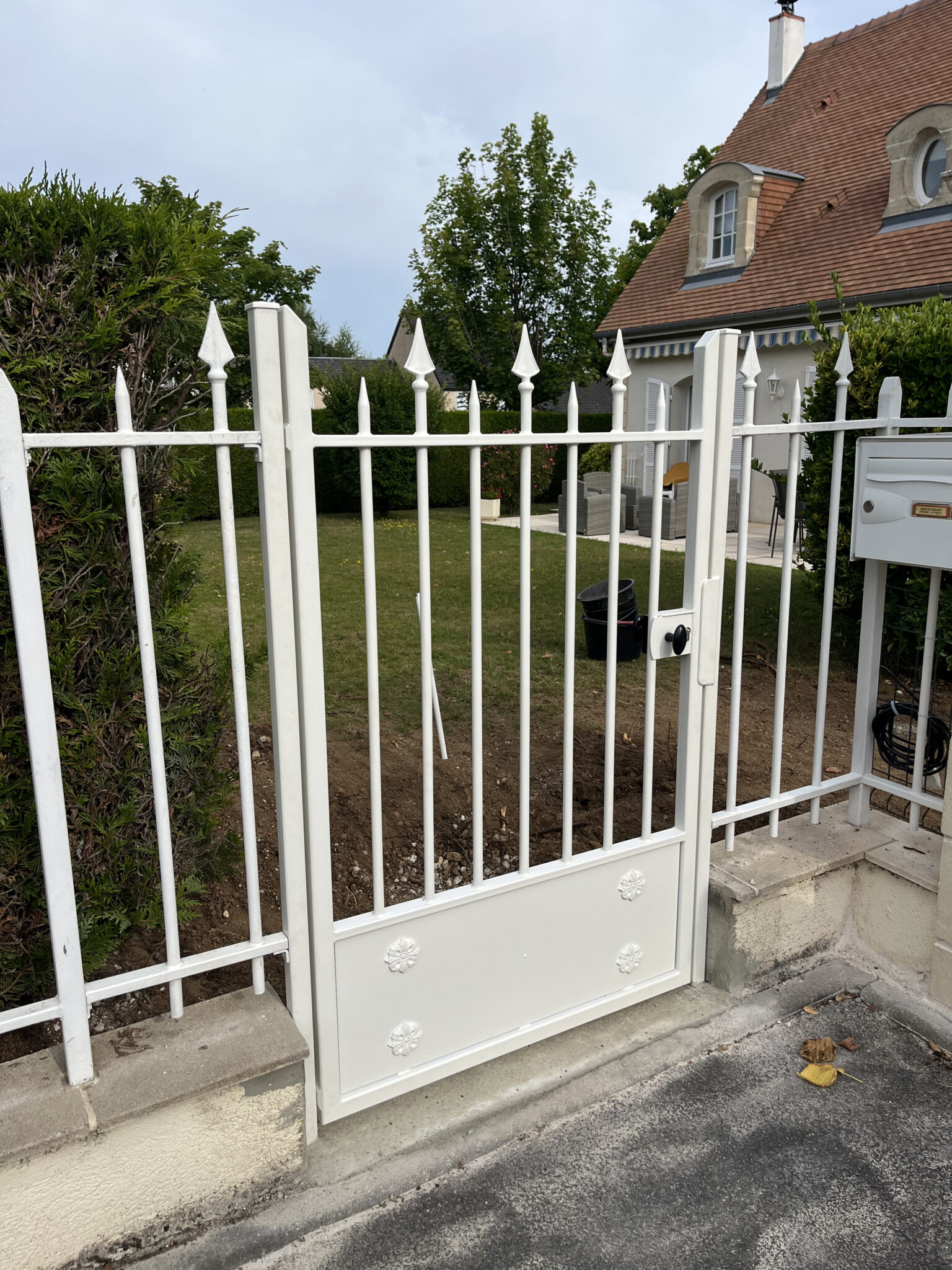 Portail blanc devant maison avec jardin.
